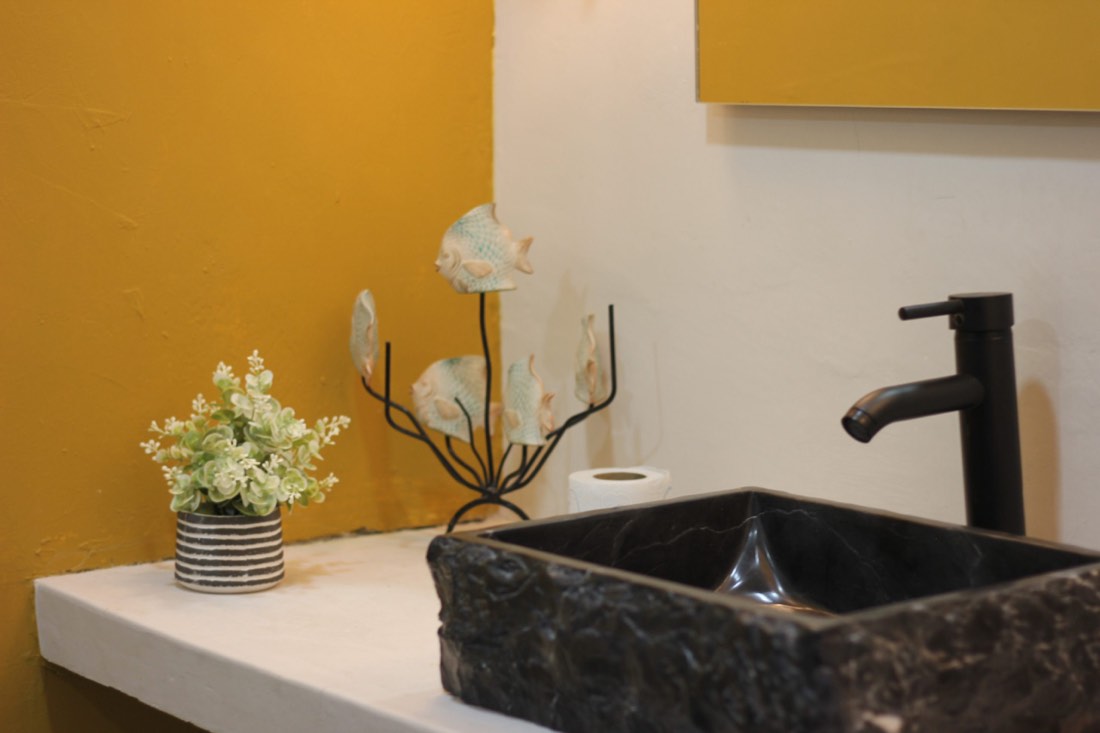 Lavabo de piedra volcánica sobre muro amarillo